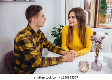 Concept of close connection. Loving girl and boy sitting in a cafe, holding one another hands, keeping eye contact, looking as if there is nothing except them in the world.