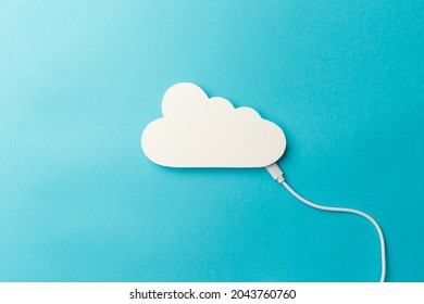 The concept of cloud technologies, cloud storage. A white cable is connected to a cloud on a blue background. Top view. Flat lay. Close-up. Copy space. Transferring data to cloud storage