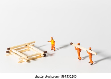 The concept of a collective solution to any problem. Miniature toy workers build a house from matches. Workers perform disposal of the Chief. Close-up view.