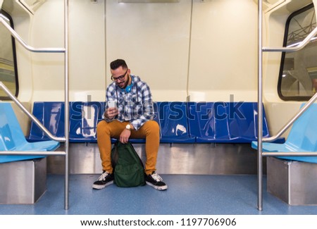 Concept of commute, urban life, aspirations, concentration, journey. Handsome commuter student man on smartphone using app texting sms message inside train compartment.