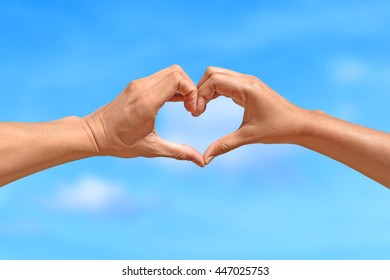 Concept or conceptual human male or man and woman hands in love, symbol of heart over blue sky background