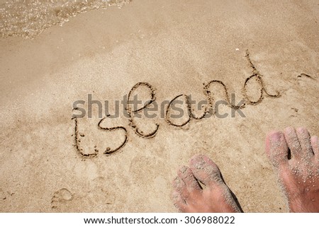 Concept or conceptual island text handwritten in sand on a beach with feet in an exotic island for tropical, summer, sea, ocean, calendar, travel, holiday, sunny, tourism, resort, time or relaxet