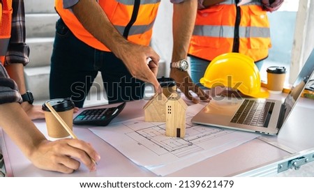 Concept construction Engineer, group architect meeting On the desk with a blueprint in the office, constuctions site,house model,labtop,hardhat,vest.
Teamwork to design a house on blueprints.Leader.