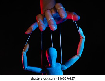 Concept of control. Marionette in human hand. Objects are colored on red and blue light.