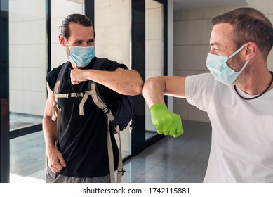 Concept: Coronavirus, Covid-19. Two Male Friends Greeting Each Other With Their Elbows At The Entrance Of A Building. New Normality, Pandemics And Epidemics Prevention.