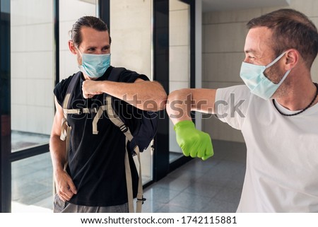Concept: Coronavirus, covid-19. Two male friends greeting each other with their elbows at the entrance of a building. New normality, pandemics and epidemics prevention.