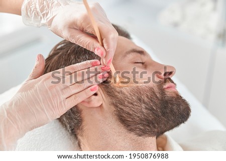 Concept of cosmetology and facial. A woman beautician makes face and beard modeling for a man waxing epilation. Depilation with wax