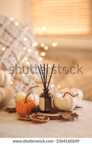 Concept of cozy fall home atmosphere, aromatherapy. Perfume, appartment aroma diffuser with autumn scent of pumpkin spicy latte, cinnamon, anise. Room decor with pumpkins, dry orange, wool plaid