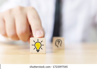 Concept creative idea and innovation. Hand choose wooden cube block with light bulb icon and blurred question mark symbol