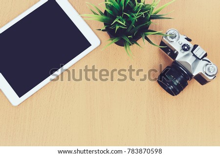 Concept of creative workplace - top view of retro slr camera, green flower and digital tablet on a wooden desk ( vintage effect)