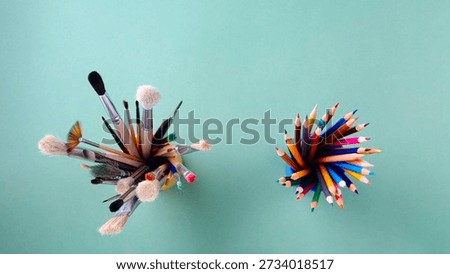 Concept for creativity, art, and development. Top view:  glass with various sized and colored paintbrushes and glass with multicolored pencils on green background. Above  spaces for drawing, writing, or text. back to school