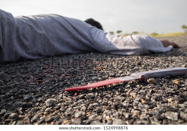 Concept of Crime murder scene, Selective focus of bloody knife on the road with dead body as background lying on Road