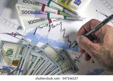 Concept Of Currency Trading. Hundred Us Dollar Bills Lying . Packs Of Euro  Bills. Currency Us Euro Rate Chart Under The Bills. Male Hand With Pen Above Charts.