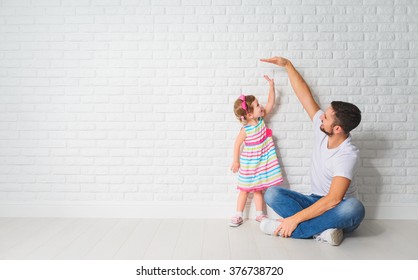 concept  Dad measures the growth her child daughter at blank brick wall