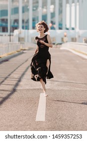 Concept Dancepics Outdoors Dance And Female Beauty. Beautiful Brunette Woman In Black Dress And Pointe Dancing Over City Background. Running Towards The Camera Close Up View