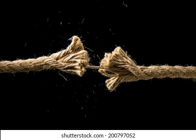 Concept Of Danger And Risk With Two Ends Of A Frayed Worn Rope Held Together By The Last Strand On The Point Of Snapping, Against A Dark Background With Copyspace.