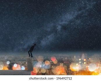 Concept Of Dangerous Balance, Business Man Dancing On A Stone Of The Roof Of City Under Stars In Night.