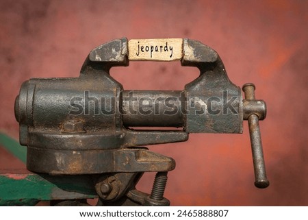 Concept of dealing with problem. Vice grip tool squeezing a plank with the word jeopardy