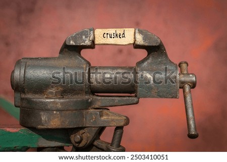 Concept of dealing with problem. Vice grip tool squeezing a plank with the word crushed
