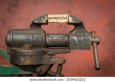 Concept of dealing with problem. Vice grip tool squeezing a plank with the word uncomplicated