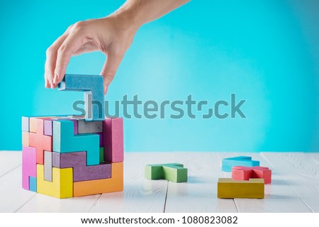 Concept of decision making process, logical thinking. Logical tasks. Conundrum, find the missing piece of the proposed. Hand holding wooden puzzle element. Hand sets the last element of the puzzle. 