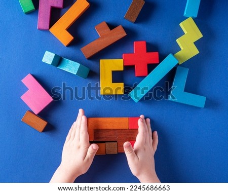 Concept of decision making process, logical thinking. Find the missing piece of the proposed. Children's hands hold puzzle element. Background with colorful shapes wooden blocks