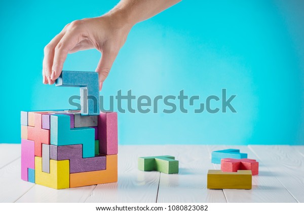 Concept of decision making process, logical thinking.\
Logical tasks. Conundrum, find the missing piece of the proposed.\
Hand holding wooden puzzle element. Hand sets the last element of\
the puzzle. 