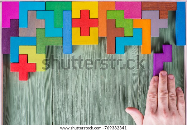 Concept of decision making\
process, logical thinking. Find the missing piece of the proposed.\
Hand holding puzzle element. Background with colorful shapes wooden\
blocks
