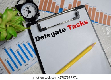 Concept of delegate tasks write on clipboard with financial graphs isolated on Wooden Table.