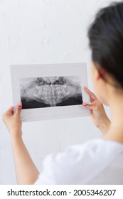 Concept Dentistry. Blur Doctor Watches To Black And White Picture. From Behind Of Young Woman Dentist With Black Hair Looks At Snapshot Of Teeth. Vertical Photo, Story Instagram With Copyspace.