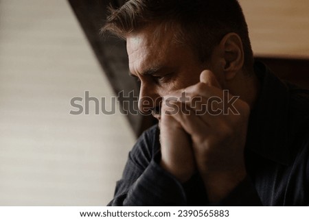 Concept of depression. Mid shot adult man clasped arms and thinking about religion. Young male prayer folded hands together minded. Religious guy begs for his acquired sins. Thoughtful person