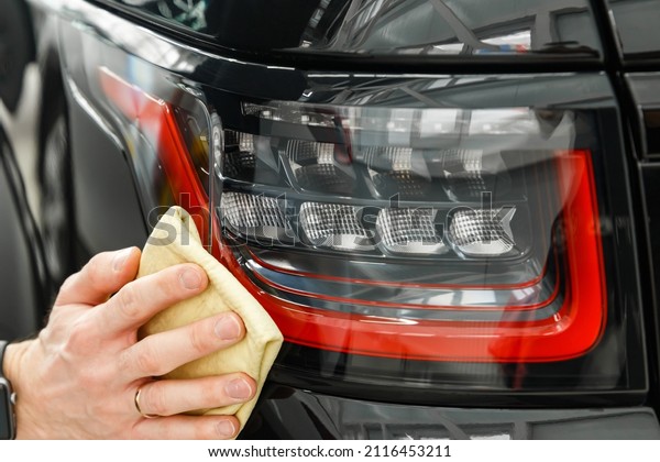 The concept of\
detailing the car. Car detailing - a man holds a microfiber cloth\
in his hand and polishes the car. Cleaning the rear lights of the\
car in close-up.
