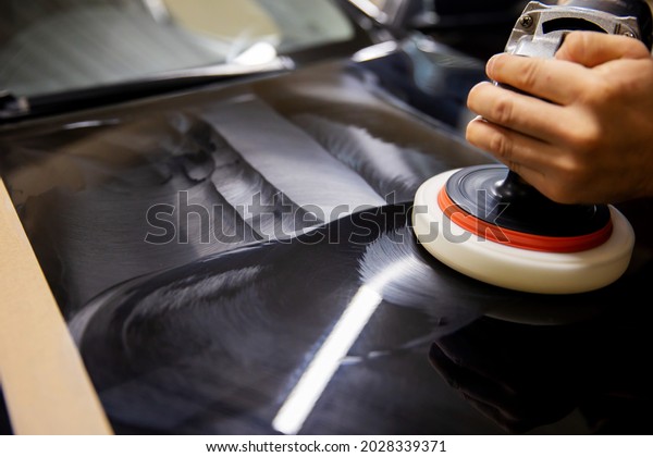 The concept of detailing and polishing cars.\
The hands of a professional car service worker, with an orbital\
polisher, polish the black luxury hood of a car in an auto repair\
shop. car polishing