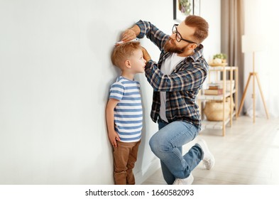 Concept Of Development, Growing Up. A Father Measures Height Of His Young Child Son
