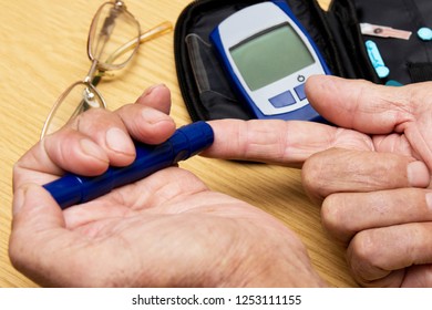 Concept Diabetes In The Elderly Retired. Senior Man With Glucometer Checking Blood Sugar Level At Home. Learn To Use A Glucometer