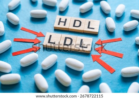 Concept of the difference between HDL and LDL cholesterol, words composed with wooden alphabet on a blue background, and drug tablets surrounding them; bad LDL cholesterol.