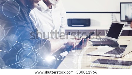 Concept of digital screen,virtual connection icon,diagram,graph interfaces.Bearded young man holding mobile phone and touching display.Adult businessman working together with partner.Film effect,wide.