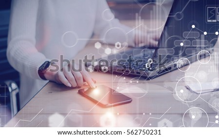Concept of digital screen,virtual connection icon,diagram,graph interfaces.Pensive young beautiful businesswoman using modern mobile phone and laptop while sitting at her working place.Flares