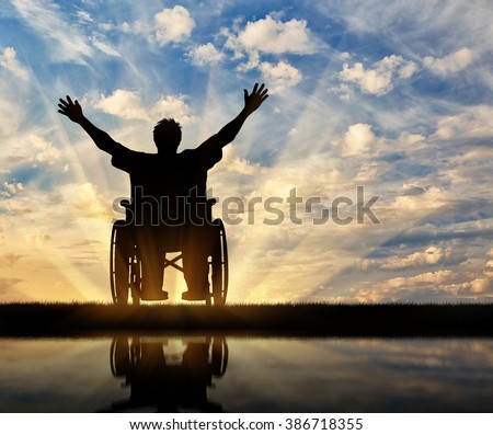 Concept of disability and disease. Silhouette happy disabled person in a wheelchair at sunset and reflection in water