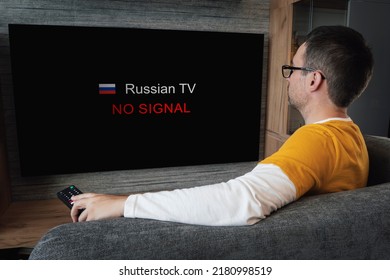 The Concept Of Disconnecting Russian Channels In Europe And The USA. Blocking Of Russian TV Broadcasting. Young Handsome Man Watching TV On A Sofa At Home.