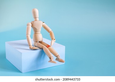 The concept of diseases of the knee joint. The figure of a wooden man on a blue podium with the knee of the leg highlighted in red on a light background.