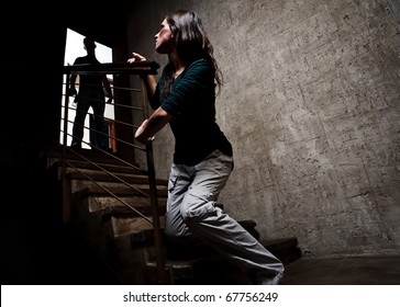 Concept of domestic abuse. Battered woman escaping from man silhouetted at the top of the stairs, in fear of more violence