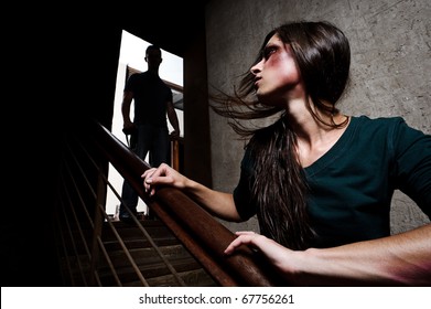 Concept of domestic abuse. Battered woman escaping from man silhouetted at the top of the stairs, in fear of more violence