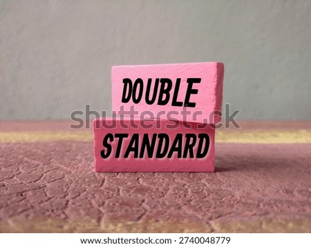 Concept of Double Standards represented by unbalanced pink wooden blocks on textured background.