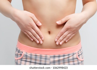 Concept Of Early Term Of Pregnancy. Close Up Photo Of Woman's Abdomen And Belly Button, She Is Touching Her Slim Stomach With Two Hands. Isolated On White Background
