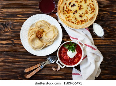 The Concept Of Eastern European National Cuisine. Ukrainian, Russian, Polish Food.Traditional Beetroot Soup Borscht With Sour Cream, Pancakes Blini, Dumplings Vareniki With Potatoes And Fried Onions