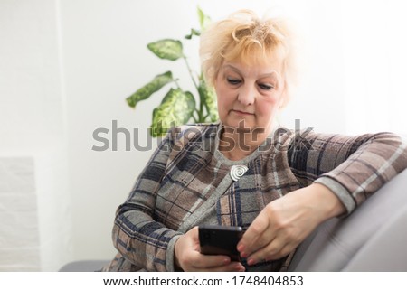 Concept of easy, fast usage of modern technology among all ages. Portrait of confident mature woman with wrinkles she is using her modern smartphone for sending a message isolated on gray background