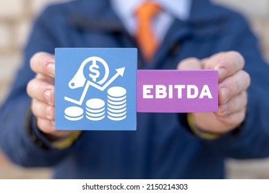 Concept of EBITDA - Earnings Before Interest Taxes Depreciation Amortization. Businessman holding colorful foam plastic blocks with EBITDA abbreviation and growing chart icon.
