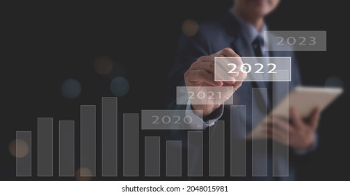 Concept Of Economic Recovery In Year 2022 After The Fall Due To The Covid 19 Coronavirus Pandemic. Businessman Pointing 2022 Button With Increase Graph Corporate Future Growth Plan And Business Goals