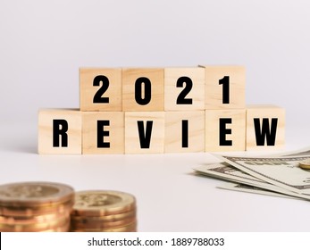 Concept of economy and business.Phrase 2021 REVIEW on wooden cubes with magnifying glass,coins and dollar bills isolated on white background.